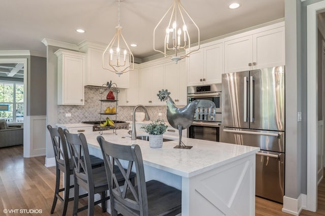 kitchen featuring a kitchen island with sink, hanging light fixtures, light stone countertops, appliances with stainless steel finishes, and white cabinetry