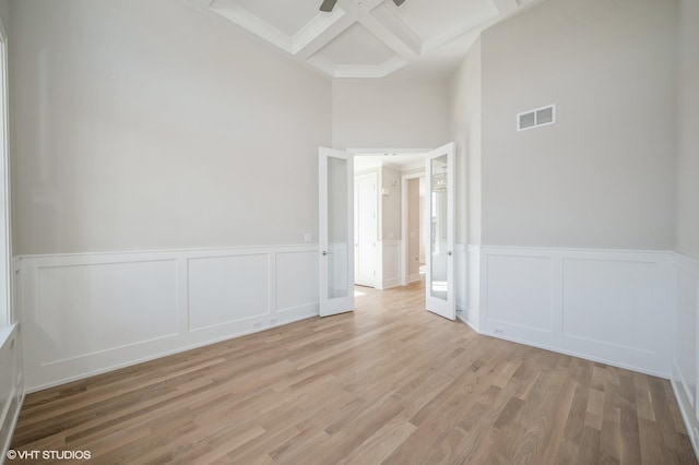 unfurnished room featuring beam ceiling, a high ceiling, coffered ceiling, and light hardwood / wood-style floors