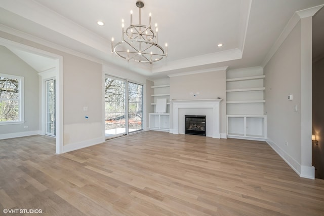 unfurnished living room featuring a chandelier, light hardwood / wood-style floors, a raised ceiling, and crown molding