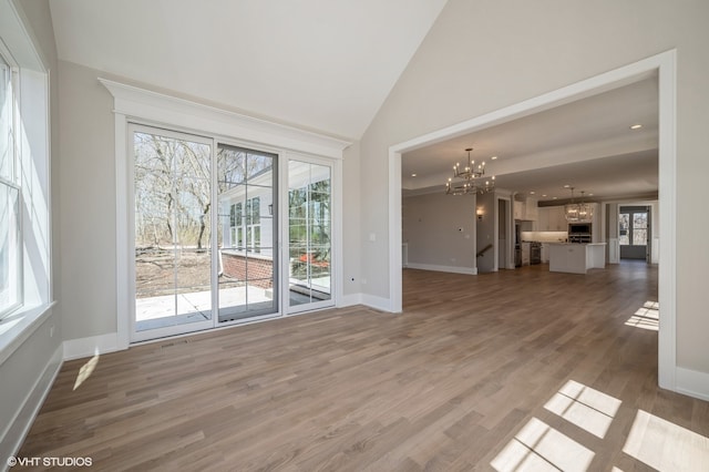 unfurnished living room with high vaulted ceiling, an inviting chandelier, and hardwood / wood-style flooring