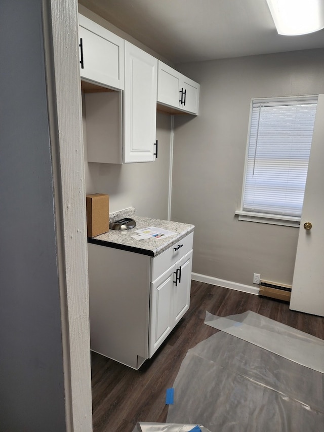 kitchen with white cabinets, dark hardwood / wood-style flooring, light stone counters, and baseboard heating