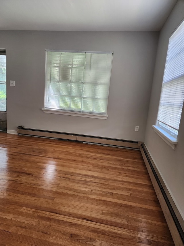 spare room with hardwood / wood-style flooring, baseboard heating, and a healthy amount of sunlight