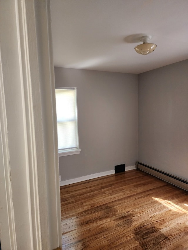 unfurnished room featuring hardwood / wood-style floors and a baseboard heating unit