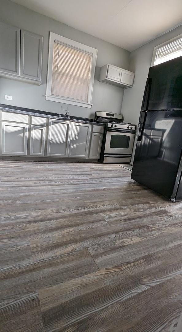 kitchen with black fridge, wood-type flooring, ventilation hood, stainless steel range with gas cooktop, and white cabinets