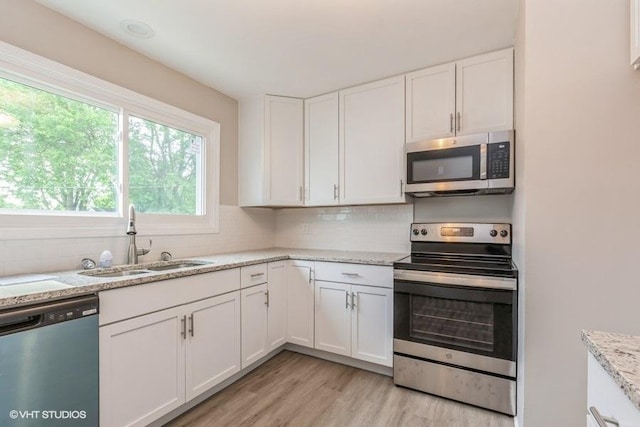 kitchen with white cabinets, sink, light hardwood / wood-style flooring, light stone countertops, and stainless steel appliances