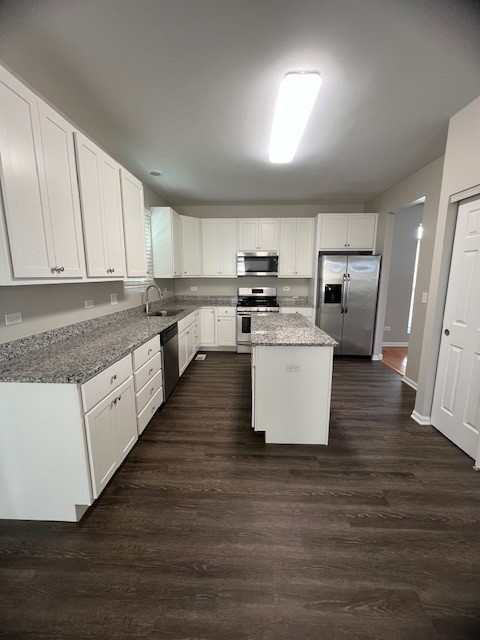 kitchen with a kitchen island, white cabinetry, stainless steel appliances, sink, and light stone counters