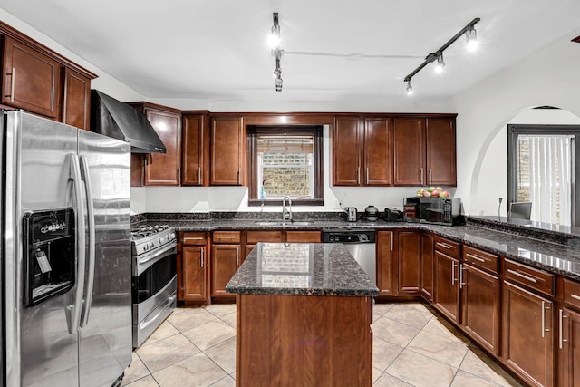 kitchen featuring a center island, sink, wall chimney exhaust hood, stainless steel appliances, and dark stone counters