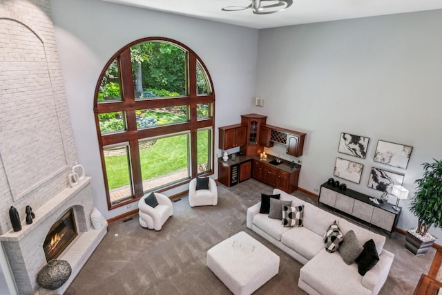 living room featuring a brick fireplace, dark carpet, plenty of natural light, and a high ceiling