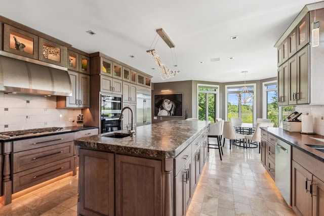 kitchen featuring dark stone counters, tasteful backsplash, stainless steel appliances, pendant lighting, and a center island with sink