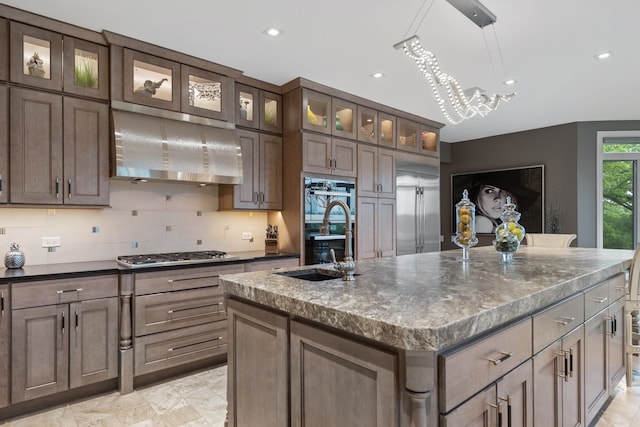 kitchen with tasteful backsplash, stainless steel appliances, a center island with sink, light tile patterned floors, and wall chimney exhaust hood