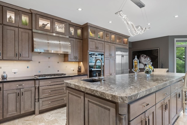 kitchen with pendant lighting, sink, appliances with stainless steel finishes, a kitchen island with sink, and ventilation hood