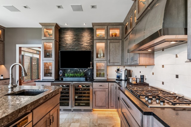 kitchen featuring wine cooler, stainless steel gas cooktop, wall chimney exhaust hood, decorative backsplash, and sink