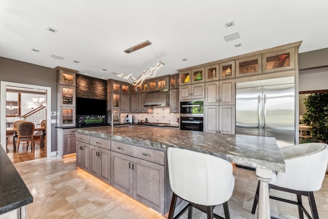 kitchen featuring dark stone counters, stainless steel appliances, wall chimney range hood, pendant lighting, and a center island