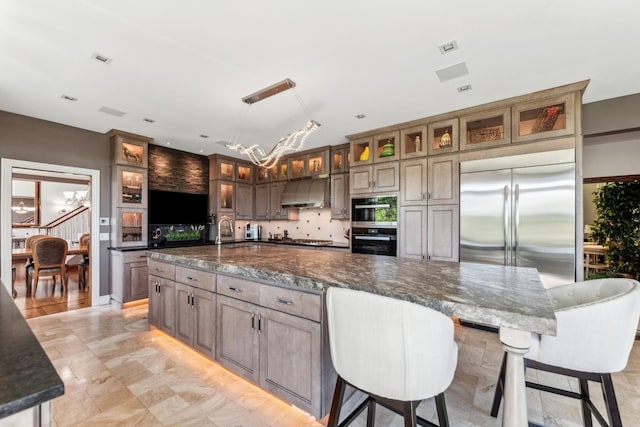 kitchen with hanging light fixtures, stainless steel appliances, a spacious island, dark stone counters, and a chandelier