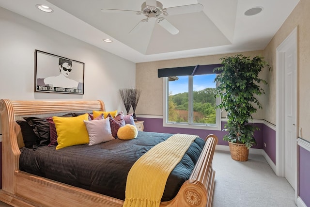 carpeted bedroom with ceiling fan and a raised ceiling