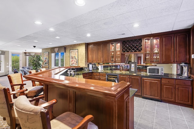 kitchen with light tile patterned flooring, a breakfast bar, kitchen peninsula, beverage cooler, and a paneled ceiling