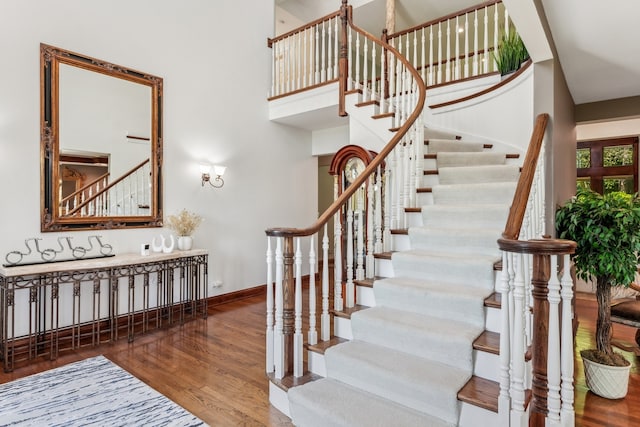 staircase with wood-type flooring and a towering ceiling