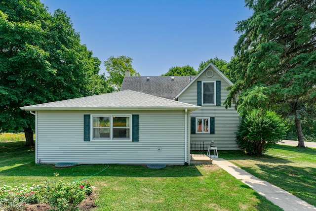 rear view of house with roof with shingles and a lawn