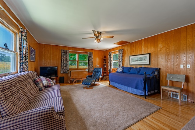 living area with visible vents, ceiling fan, wood walls, and wood finished floors