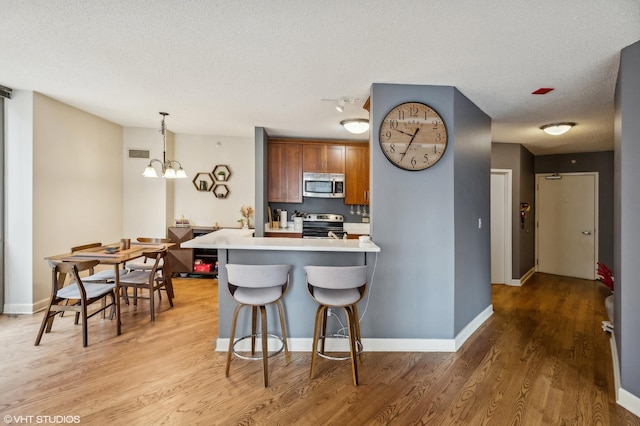 kitchen with a textured ceiling, stainless steel appliances, decorative light fixtures, an inviting chandelier, and light hardwood / wood-style flooring