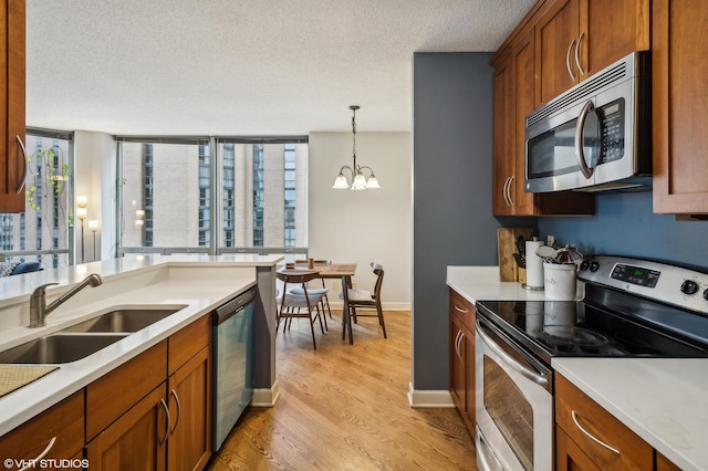 kitchen with pendant lighting, sink, a textured ceiling, appliances with stainless steel finishes, and a chandelier