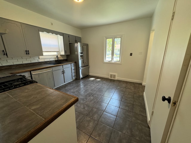 kitchen featuring stainless steel appliances, decorative backsplash, dark tile patterned flooring, sink, and gray cabinets