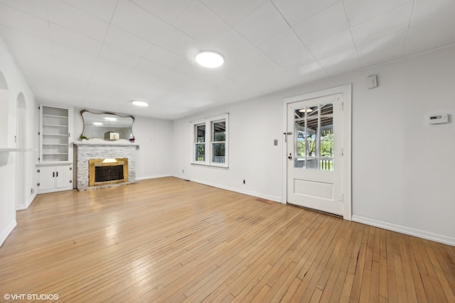 unfurnished living room with a stone fireplace, light hardwood / wood-style floors, built in features, and plenty of natural light