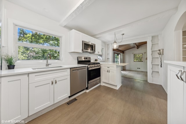 kitchen featuring dark wood-type flooring, lofted ceiling with beams, appliances with stainless steel finishes, white cabinets, and sink