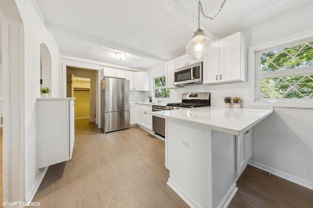 kitchen featuring light hardwood / wood-style floors, stainless steel appliances, white cabinets, kitchen peninsula, and decorative light fixtures