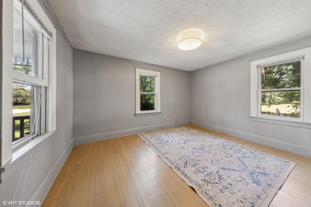 empty room with light hardwood / wood-style floors, a wealth of natural light, and a textured ceiling