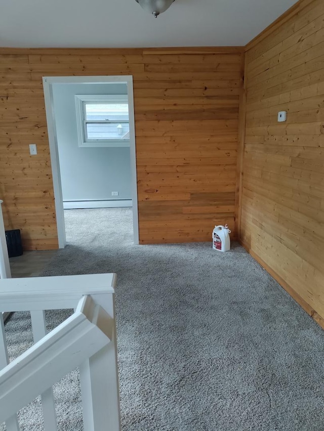 carpeted spare room featuring baseboard heating and wood walls