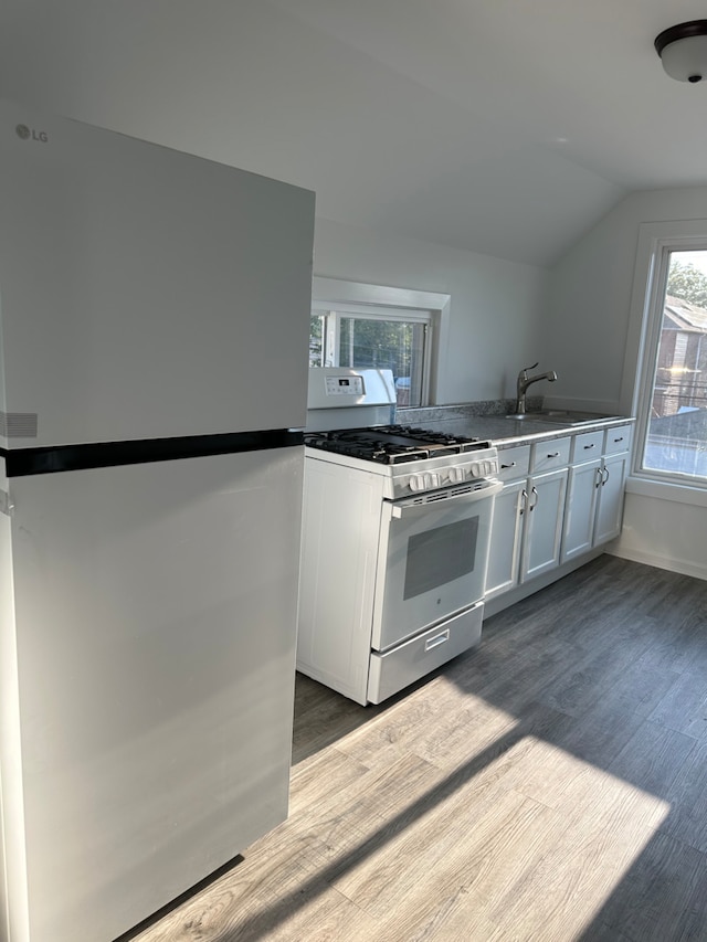 kitchen with vaulted ceiling, stainless steel fridge, white gas stove, white cabinetry, and wood-type flooring