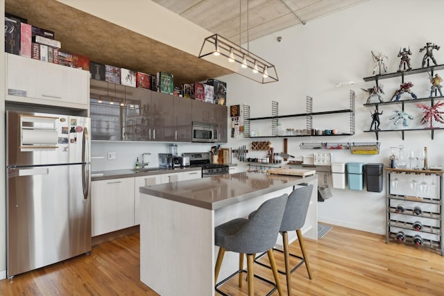 kitchen with a center island, light hardwood / wood-style floors, a breakfast bar, white cabinets, and appliances with stainless steel finishes