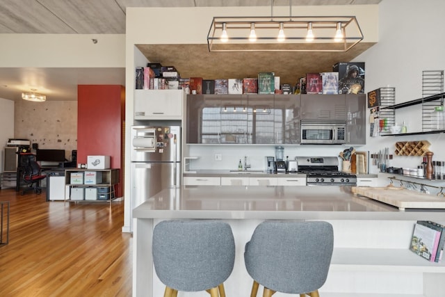 kitchen featuring white cabinetry, sink, hanging light fixtures, stainless steel appliances, and light hardwood / wood-style floors