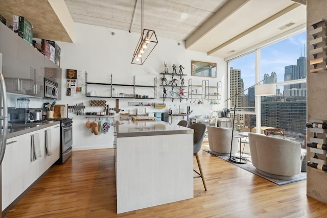 kitchen featuring hardwood / wood-style floors, white cabinets, hanging light fixtures, a kitchen bar, and stainless steel appliances