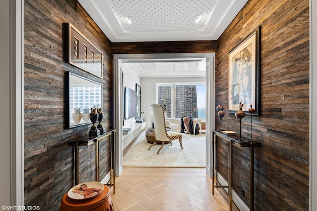 corridor with a tray ceiling, light parquet floors, and wooden walls