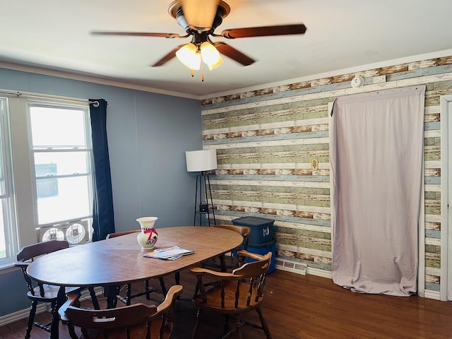 dining room with dark wood-type flooring, ceiling fan, crown molding, and wooden walls