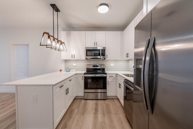 kitchen featuring kitchen peninsula, hanging light fixtures, appliances with stainless steel finishes, tasteful backsplash, and white cabinetry