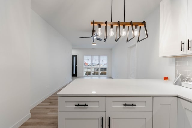 kitchen with kitchen peninsula, light wood-type flooring, white cabinetry, and backsplash