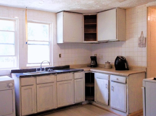 kitchen with sink, white cabinetry, backsplash, light hardwood / wood-style floors, and washer / dryer