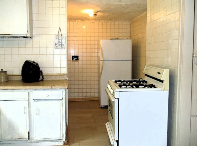 kitchen with tile walls, white appliances, light hardwood / wood-style floors, and white cabinetry