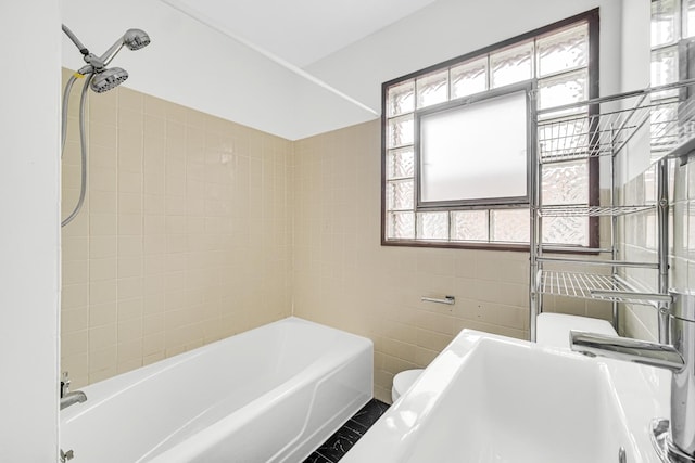 bathroom featuring tiled shower / bath combo, toilet, and tile walls