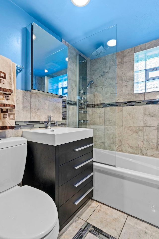 full bathroom featuring tile walls, vanity, tiled shower / bath, decorative backsplash, and toilet