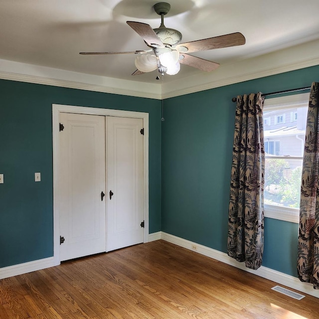 unfurnished bedroom with hardwood / wood-style floors, a closet, ceiling fan, and crown molding