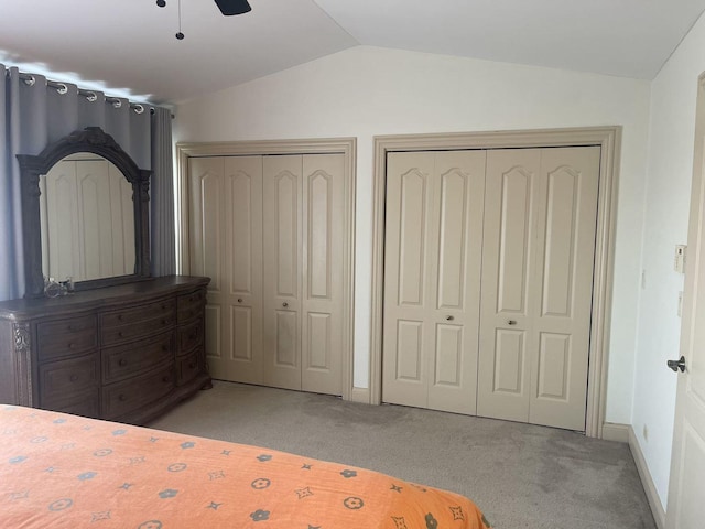 unfurnished bedroom featuring light carpet, vaulted ceiling, and multiple closets