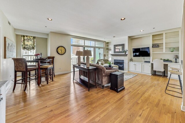 living room with a tile fireplace, light wood-type flooring, and built in shelves