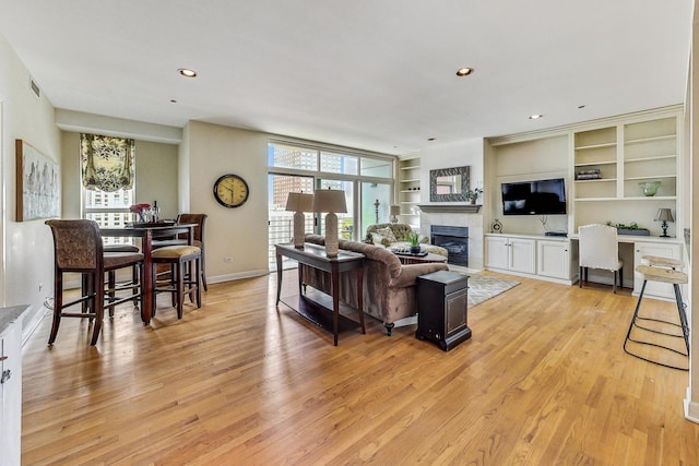 living room featuring a tile fireplace, built in desk, built in features, and light hardwood / wood-style floors