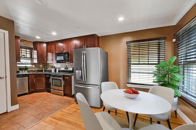 kitchen with a wealth of natural light, stainless steel appliances, decorative backsplash, and light hardwood / wood-style floors