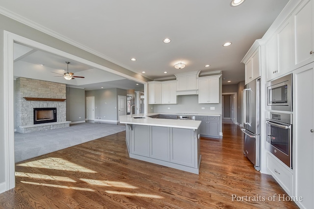 kitchen with white cabinets, a stone fireplace, sink, an island with sink, and stainless steel appliances