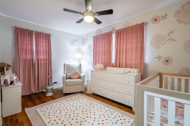 bedroom featuring a nursery area, ceiling fan, and wood finished floors